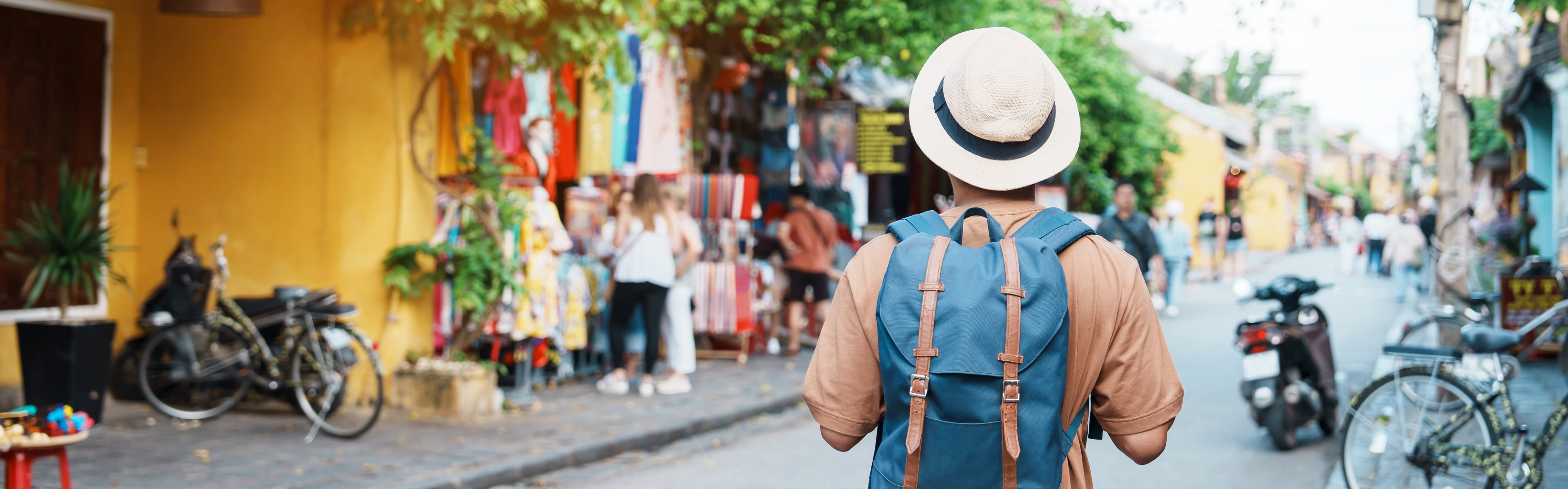 帽子をかぶりリュックを背負った人物がカラフルな街並みを歩いている後ろ姿