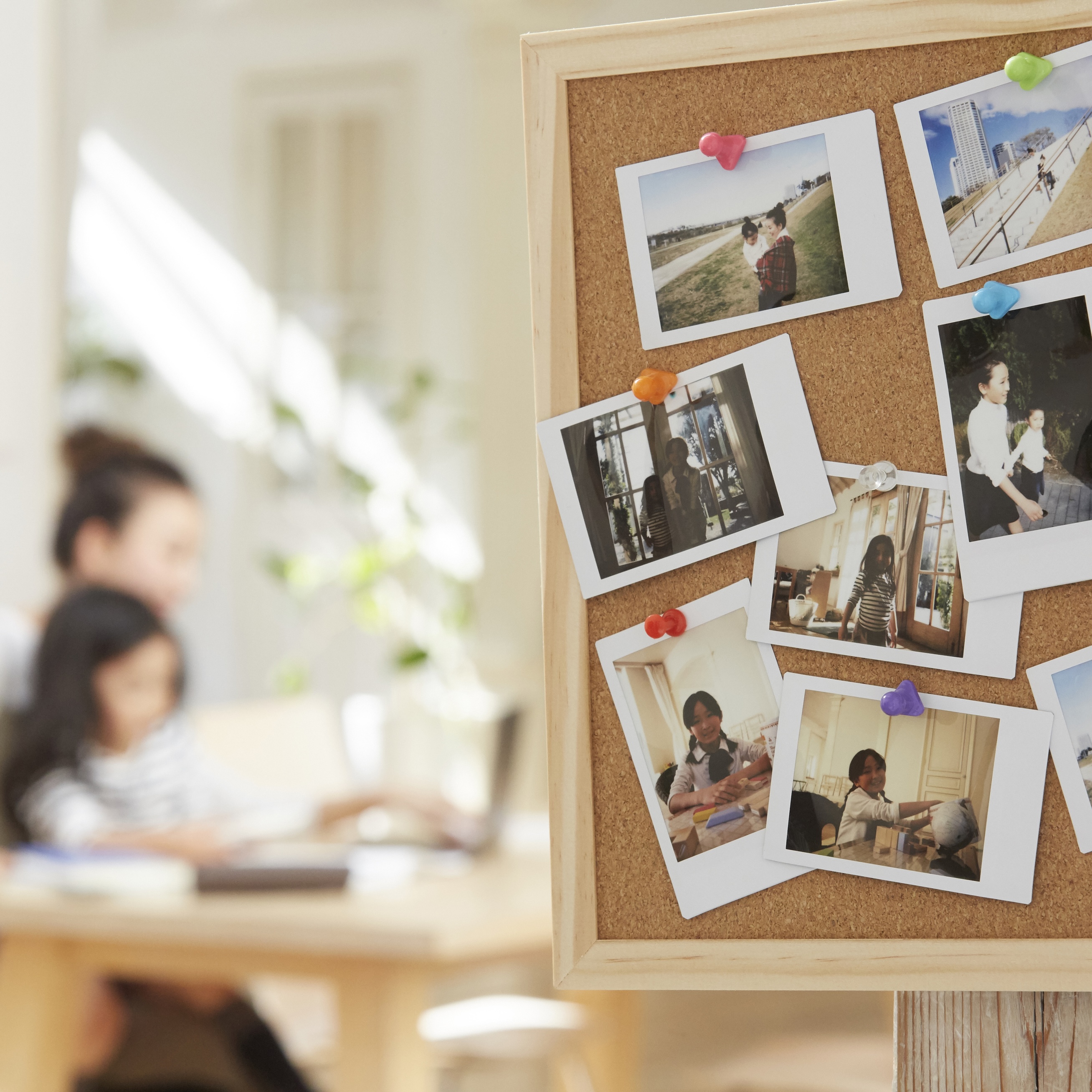 コルクボードに複数のインスタント写真がカラフルなピンで留められている