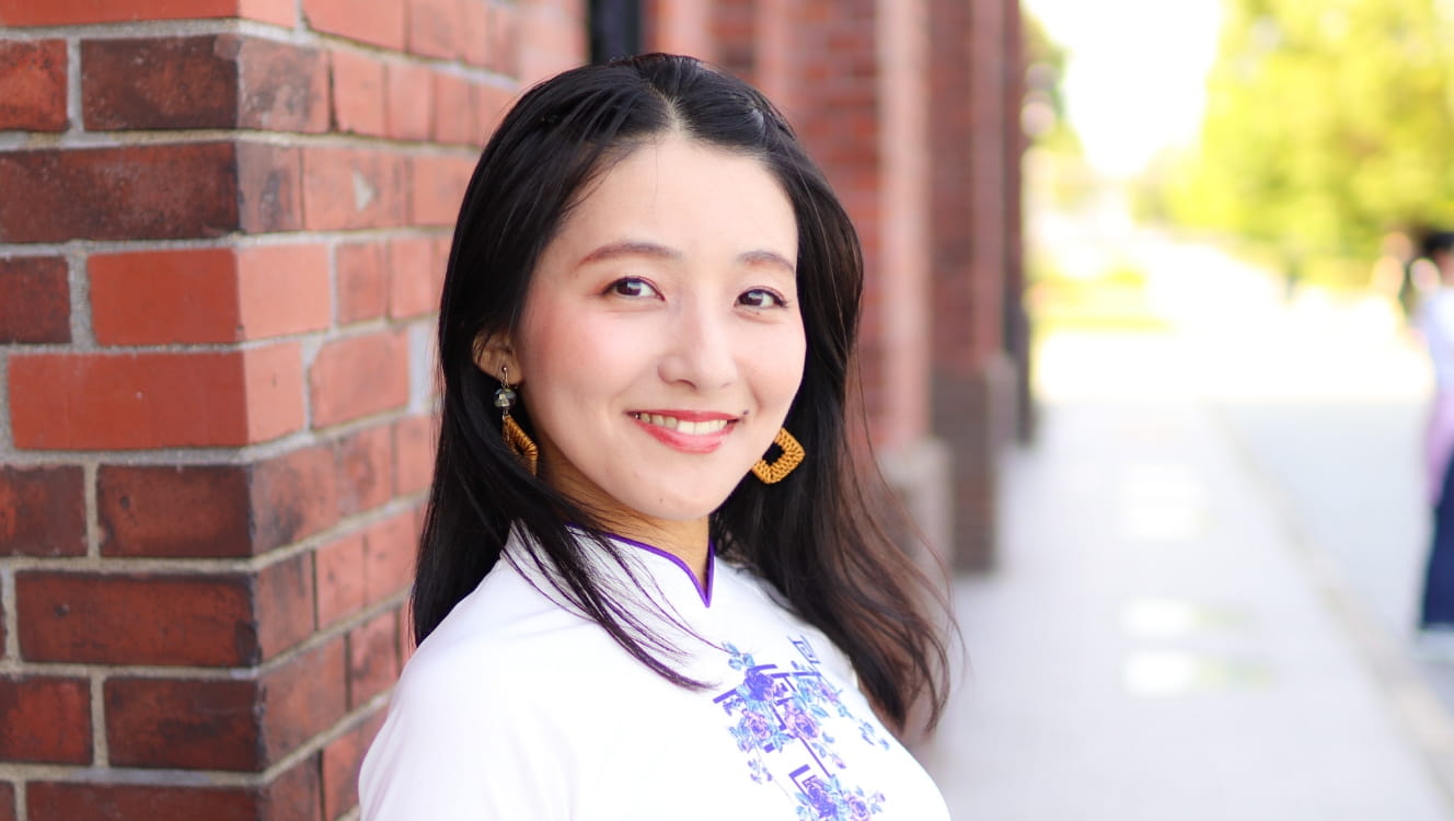 レンガ造りの建物の前で微笑むアオサイを着た女性がカメラを見つめている