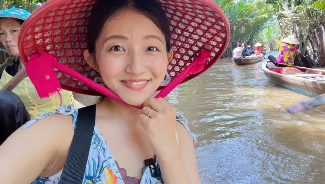 大きな赤い編み笠をかぶった女性が川の上で自撮りしている